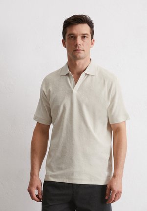 Lichtbeige polo shirt van een gestructureerde stof, korte mouwen en een V-hals. Eenvoudig ontwerp zonder zichtbare patronen of accenten.