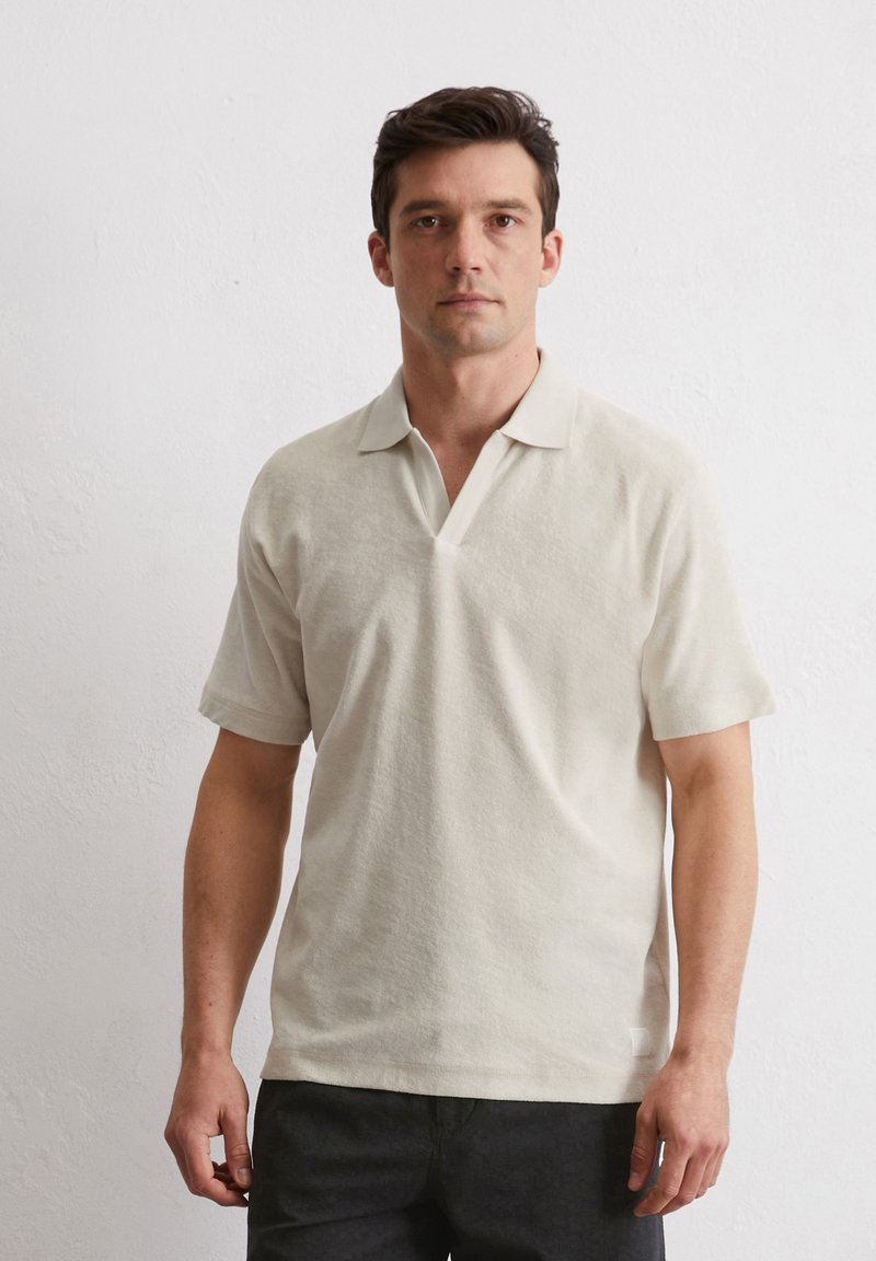 Lichtbeige polo shirt van een gestructureerde stof, korte mouwen en een V-hals. Eenvoudig ontwerp zonder zichtbare patronen of accenten.
