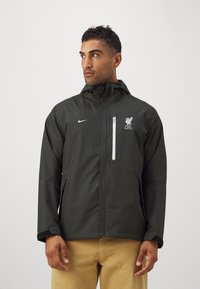 Sort vandtæt jakke med hætte, hvid frontlynlås, Liverpool FC-logo på brystet og Nike-logo på venstre side. Glat tekstur.