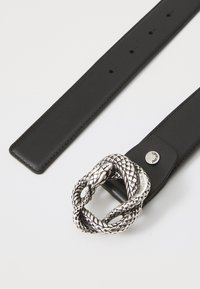 Mustapahihna, jossa on yksityiskohtainen hopeinen käärmeenkaltainen solki ja pyöreä metallinen logoakseli vyössä.