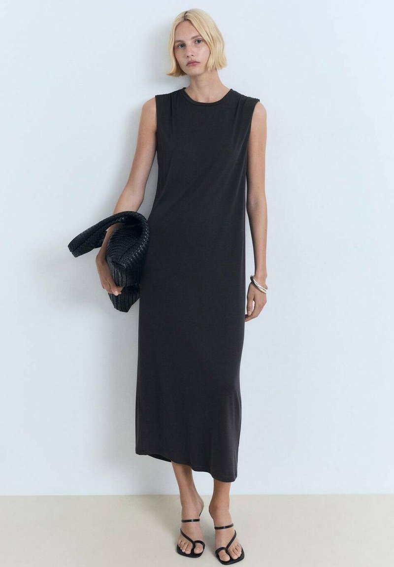 Ärmelloses, knielanges Kleid aus dunkelgrauem Jersey-Stoff, mit einem runden Ausschnitt und einer entspannten Passform. Das Model hält eine strukturierte schwarze Tasche.