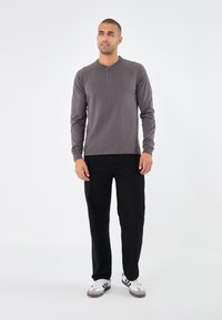Langärmliges Henley-Shirt in Dunkelgrau mit einer Drei-Knopf-Leiste und gerippten Bündchen, kombiniert mit schwarzen Hosen und weißen Sneakers.