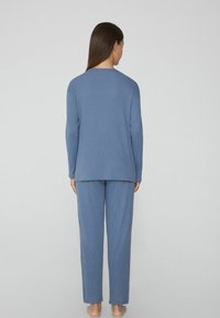 Conjunto de loungewear azul con relieve que consiste en una parte superior de manga larga y pantalones, con un corte relajado y pantalones hasta los tobillos. Textura suave.