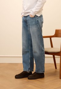 Hellblaue, weit geschnittene Jeans aus Denim mit lockerer Passform, Fronttaschen und minimaler Verwaschung, kombiniert mit schwarzen Wildledersneakern.