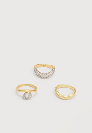 Tre guldringe på hvid overflade: én med en buet række af små diamanter, én med en pæreformet klar sten, og én simpel bånd med subtil bue.