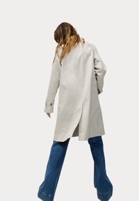 Lichtbeige trenchcoat met een achteropening, lange mouwen en knoopmanchetten, gedragen over wijde blauwe denim jeans.