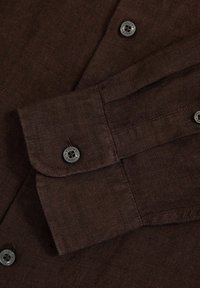 Camisa de lino marrón con puños abotonados. Presenta una textura suave y dos botones oscuros, realzados por costuras limpias.
