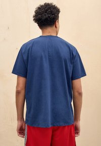 Navy blue short-sleeve t-shirt with a round neckline, featuring a relaxed fit and soft cotton texture, worn with red shorts.