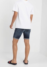 Ciemnoniebieskie szorty dżinsowe z podwiniętymi brzegami, zestawione z prostą białą koszulką i czarnymi sandałami z czerwonymi akcentami.