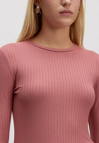 Gestreiftes Langarmoberteil aus weichem rosa Stoff. Verfügt über einen runden Halsausschnitt und eine figurbetonte Passform, die Textur und Dehnbarkeit betont.