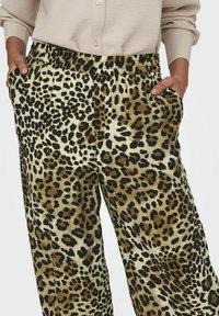 Pantaloni a motivi leopardati realizzati in tessuto morbido, dotati di cintura elasticizzata, tasche laterali e vestibilità comoda. Il design include macchie nere e marroni variegate.