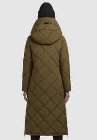 Olivegrøn lang pufferjakke med diamantquilting, hætte og sidelommer. Tekstilerne har en mat finish. Sort strikbeanie bæres.