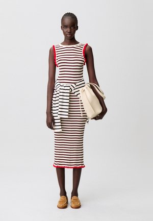 Vestido bodycon a rayas con detalles de volantes rojos, combinado con un suéter a rayas en blanco y negro atado a la cintura. Bolso beige y mocasines.