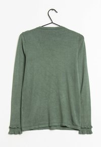 Pull vert à manches longues avec manches à volants accrochée à un cintre noir sur un fond blanc.