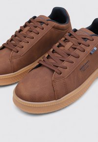 Zapatillas deportivas marrones de piel sintética con cordones planos, cuello acolchado y suela de goma. Presentan detalles con logotipo y paneles laterales texturizados.