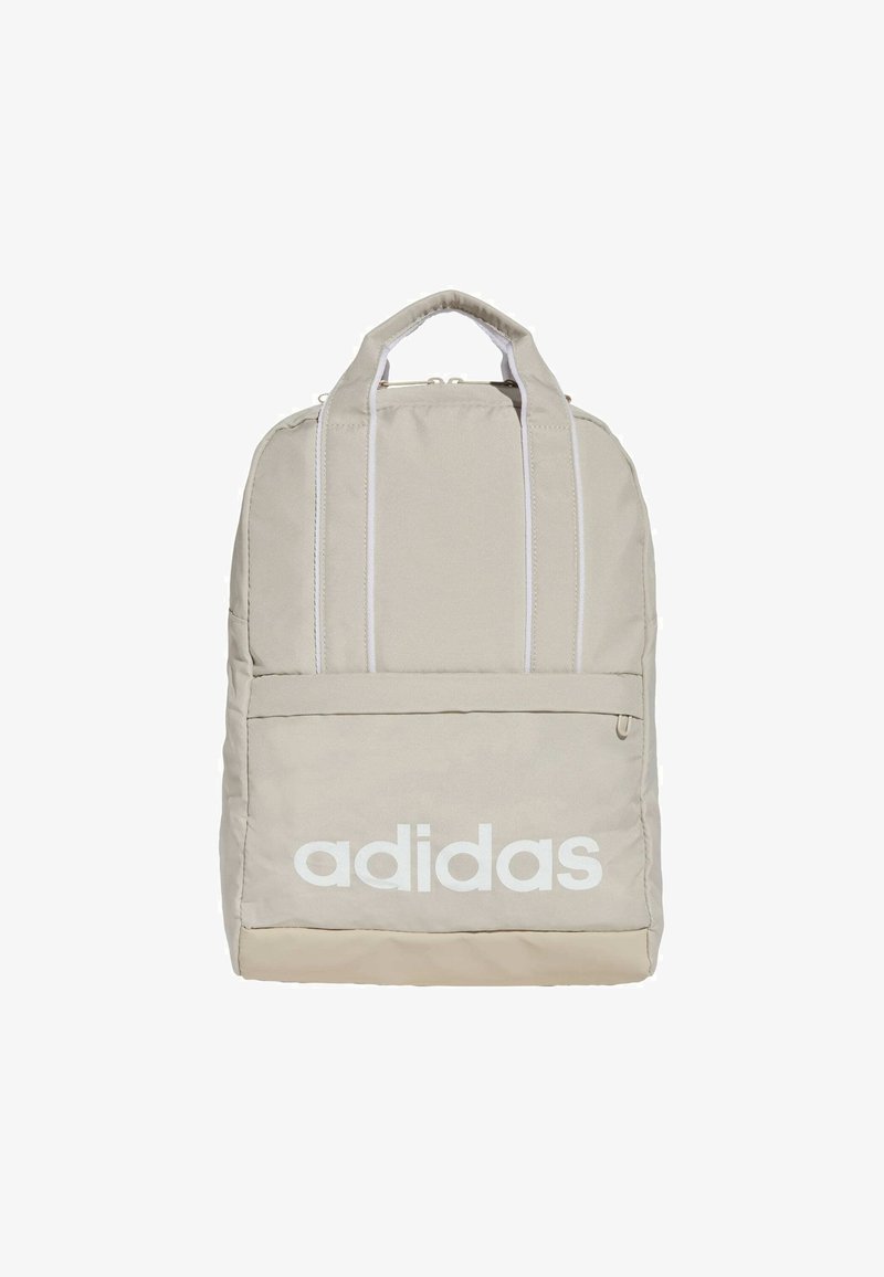 Mochila Adidas beige con una textura de tela suave, equipada con un gran bolsillo frontal y branding en blanco. Incluye dos correas de hombro acolchadas.