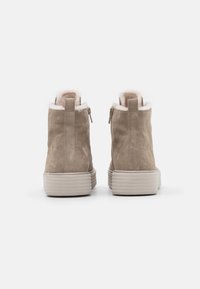 Bottines en daim beige avec une doublure blanche pelucheuse, fermeture éclair et une semelle ribbed gris clair. Le design présente une pointe arrondie.