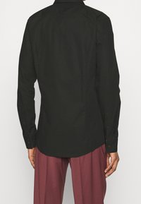 Camicia nera a maniche lunghe realizzata in tessuto liscio, con colletto a punta, polsini con bottone e orlo leggermente curvato.