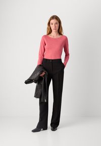 Sarkans garām piedurknēm krekls apvienots ar melniem piegrieztiem biksēm; modele tur melnu ādas jaku. Redzama gluda tekstūra un pieguļošs dizains.