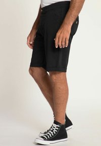 Shorts noirs avec un ourlet retourné, dotés de poches latérales et arrière. Portés avec des baskets montantes noires, affichant un look décontracté.