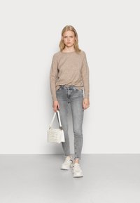 Lys brun genser, grå trange jeans, hvit crossover-veske med vevd detalj, og hvite joggesko. Antrekket har en uformell estetikk.