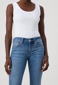 Vit ribbad linne med rundad halsringning, parat med ljusblå denimjeans med klassisk femfickdesign och knäppning.