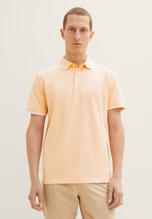 Polo en coton doux de couleur orange, avec un col blanc, une patte de boutonnage à deux boutons et un logo discret sur la poitrine. Manches courtes avec des bords côtelés.