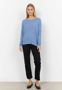 Blaues Langarmshirt mit weitem Ausschnitt, lockerer Passform und weichem Material, kombiniert mit schwarzen geraden Hosen und schwarzen flachen Schuhen.