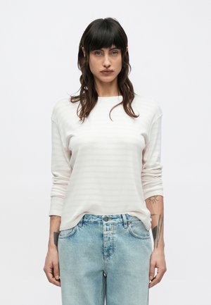 Ανοιχτό ροζ μακρυμάνικη μπλούζα με διακριτικές ρίγες, στρογγυλή λαιμόκοψη και άνετη εφαρμογή, συνδυασμένη με ανοιχτό μπλε τζιν παντελόνι.