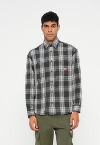 Juodai baltas languotas marškinis, pagamintas iš minkštos flanelės medžiagos, su mygtukų apykakle, krūtine kišene ir subtiliu logotipo akcentu.