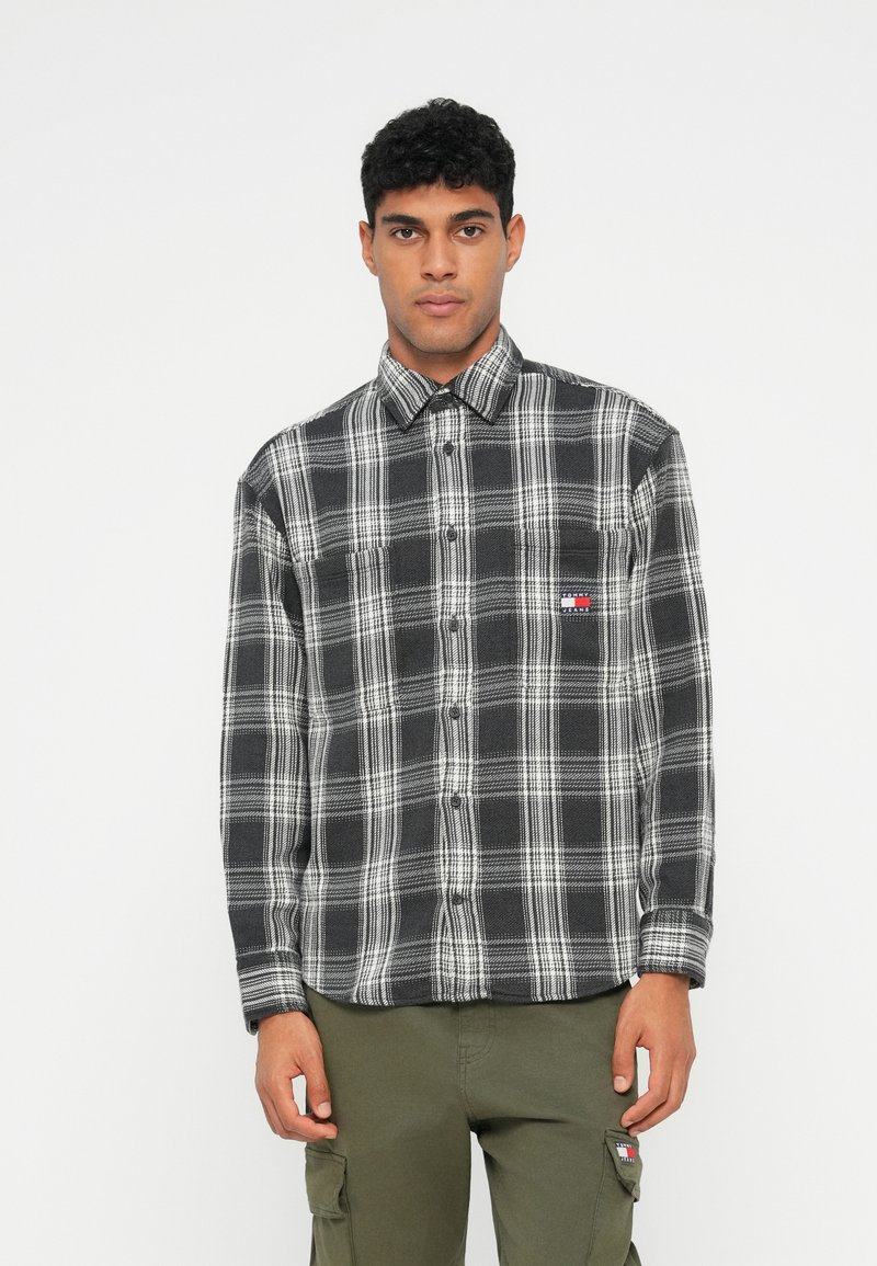 Juodai baltas languotas marškinis, pagamintas iš minkštos flanelės medžiagos, su mygtukų apykakle, krūtine kišene ir subtiliu logotipo akcentu.