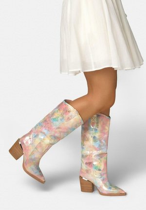 Nogi w białej spódnicy i pastelowych, wielokolorowych kowbojskich kozakach za kolano na jasnym tle.