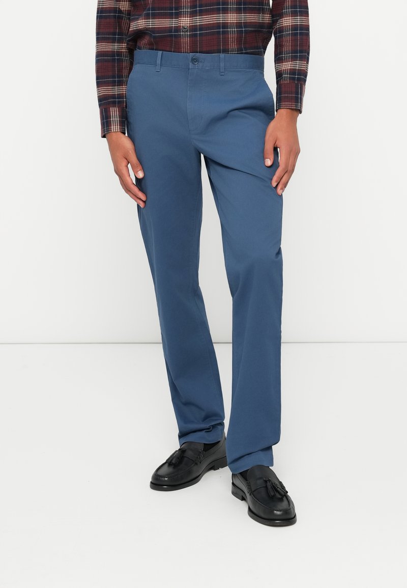 Blå bomullschinos med rett passform, har knappelukking og sidelommer, kombinert med svarte loafers. Klassisk rutete skjorte synlig.