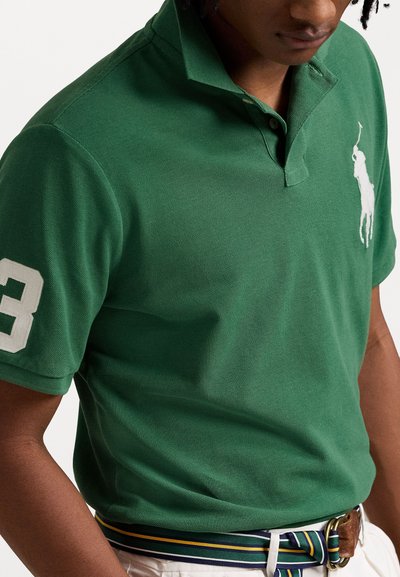Πρασινή πόλο μπλούζα φτιαγμένη από υφασματισμένο βαμβάκι, με γιακά, λευκό κεντημένο λογότυπο, και τον αριθμό 3 σε ένα μανίκι.
