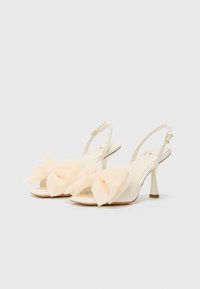 Hvite slingback hæler med en myk, blush bueaccent foran, slank hæl og en glatt tekstur med minimalistisk design.