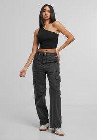 Crop top noir à une épaule associé à un pantalon cargo noir taille haute avec poches latérales, fermeture à bouton et coupe décontractée. Baskets blanches.
