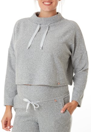 Grijze cropped sweater van zachte, gestructureerde stof met een hoge kraag en dunne grijze trekkoorden; gecombineerd met bijpassende broek met een strikceintuur.