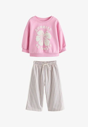 Hele roosa dressipluus valge hibiskuse graafika ja tekstiga "SUNRISE TO SUNSET". Triibulised, laia säärega püksid valge, lilla ja violettides toonides.