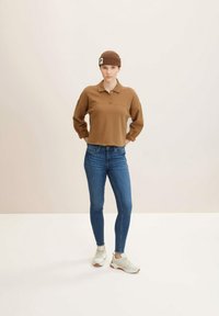 Smeđa pletena polo majica s ovratnikom, u kombinaciji s tamnoplave skinny traperice i svijetlim tenisicama. Model nosi odgovarajući smeđi vuneni šešir.