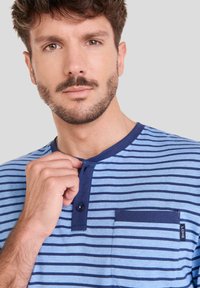 Camiseta de manga corta a rayas azul con cuello azul marino, escote abotonado y un bolsillo en el pecho izquierdo que presenta una pequeña etiqueta.