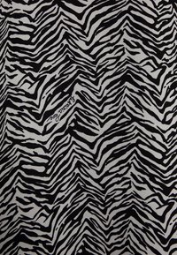 Tissu à motif zèbre avec de larges rayures noires et blanches en forme de vagues, texture lisse et un logo de marque visible dans la partie inférieure du design.
