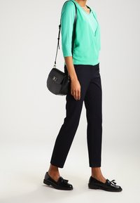 Myntgrön topp med trekvartsärmar, avslappnad passform; svarta skräddarsydda byxor; svarta loafers med rosett; liten svart crossbody-väska.