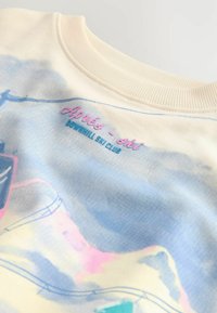 Pasztell absztrakt mintával ellátott pulóver. Bordás nyakkal, pink színű "Après-Ski" felirattal és kék "Downhill Ski Club" felirattal rendelkezik. Puha tapintású.