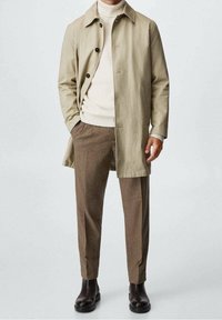 Beige puuvillane trench coat mustade nuppudega, kreemjas soonikkoes kaelus ja pruuni ruudulised püksid. Mustad pahkluu saapad lõpetavad välimuse.