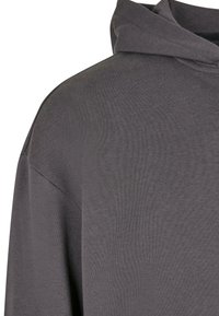 Sweat à capuche en tissu gris foncé avec une couture d'épaule visible et une capuche attachée, présenté en gros plan sur un fond blanc uni.