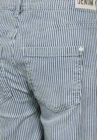 Puuvillasta valmistetut farkut, joissa on pystysuorat siniset ja valkoiset raidat. Takakuoressa on tasku ja metallinappikiinnitys taskun lähellä.