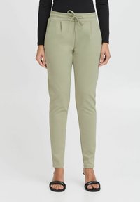 Heledad heledad rohelised püksid, millel on nööridega vöökoht, kahel esitaskul on voldid ning need on slim fit stiilis, valmistatud pehmest ja venivast materjalist.