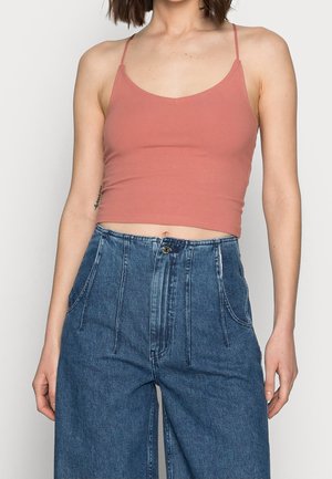 Kobieta ubrana w różowy top na ramiączkach z krótkim krojem oraz luźne, wysokowalne niebieskie dżinsy z przednimi kieszeniami.