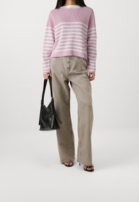 Pull en tricot rayé rose clair et blanc, coupe décontractée. Associé à un pantalon large beige. Tient un sac en cuir noir, porte des sandales noires.