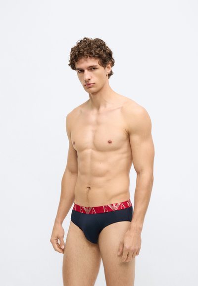 Cuecas masculinas azul-marinho com um cós elástico vermelho que exibe um padrão de logótipos. O material parece suave e elástico para maior conforto.